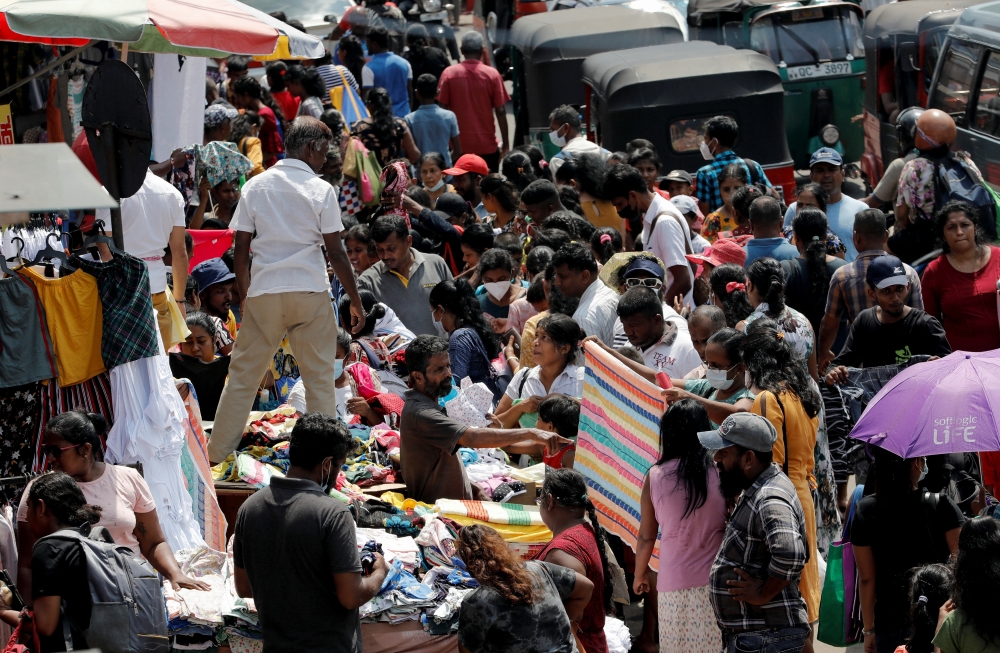 People gather around a readymade clothing stall on the side of a road to buy clothes in Colombo