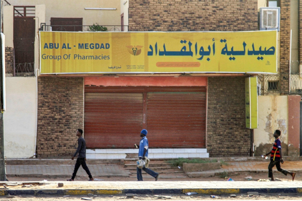 Men walk past a closed pharmacy in the south of Khartoum on April 17, 2023 as fighting in the Sudanese capital between the army and paramilitary forces led by rival generals rages for a third day.  (Photo by AFP)

