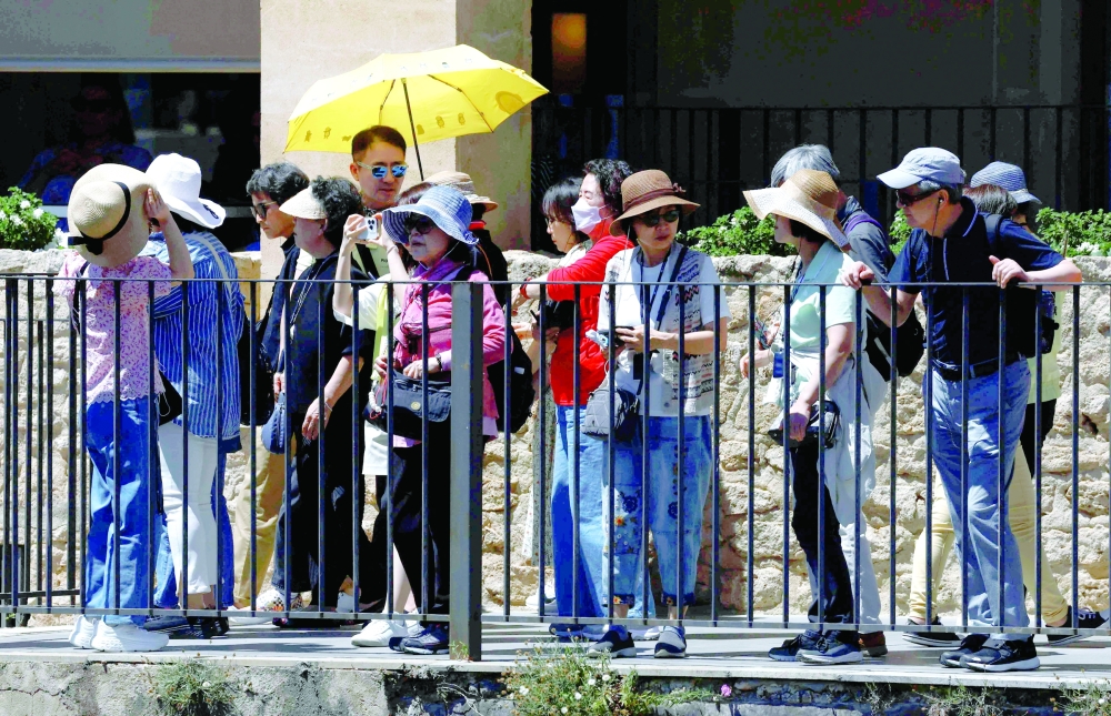 Tourists use hats and a guide uses an umbrella to protect themselves from the strong sun as they look at the New Bridge during unusually high temperatures in Ronda, Spain, on Tuesday. - Reuters