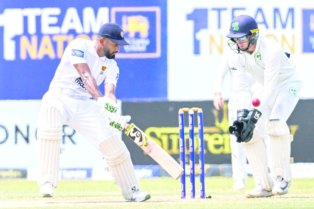 Sri Lanka's Dimuth Karunaratne (L) plays a shot as Ireland's Lorcan Tucker watches during third day of the second and final cricket Test match between Sri Lanka and Ireland at the Galle International Cricket Stadium in Galle on April 26, 2023. (Photo by Ishara S. KODIKARA / AFP)

