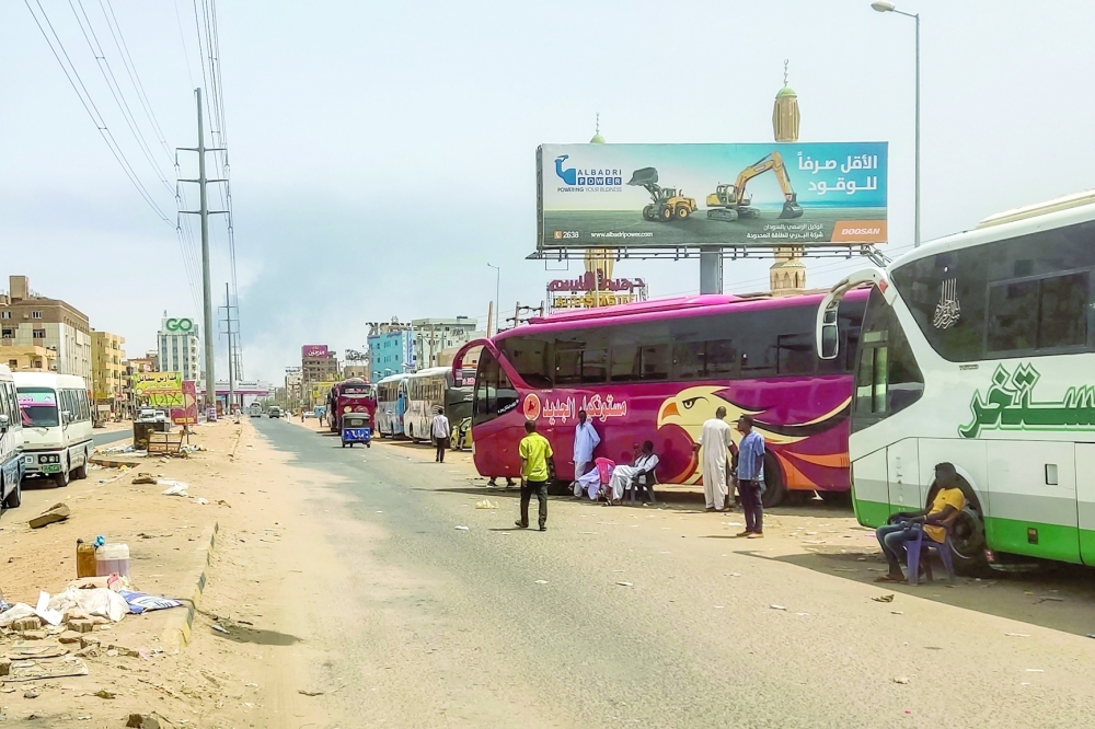 People wait next to passenger buses as smoke billows in an area in Khartoum where fighting continues between Sudan's army and the paramilitary forces on April 28, 2023. Fighting raged in Sudan on April 28, despite rival forces agreeing to extend a truce aimed to stem nearly two weeks of warfare that has killed hundreds and caused widespread destruction. (Photo by AFP)