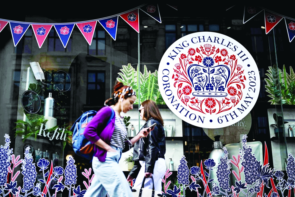 People walk past the front window of a shop decorated to celebrate the coronation weekend, in central London. The country prepares for the coronation of Britain's King Charles III and his wife Britain's Camilla, Queen Consort on May 6, 2023. - AFP