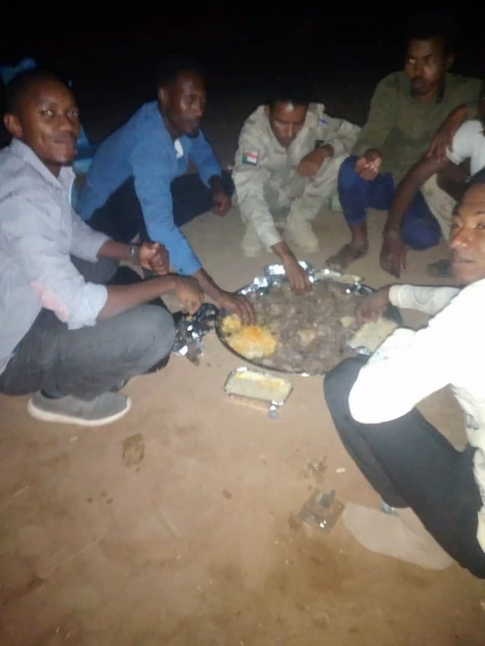 An undated photo of Sami al-Gada and Hassan Tibwa sharing a meal with soldiers of the Rapid Support Forces, a paramilitary group. (via The New York Times)