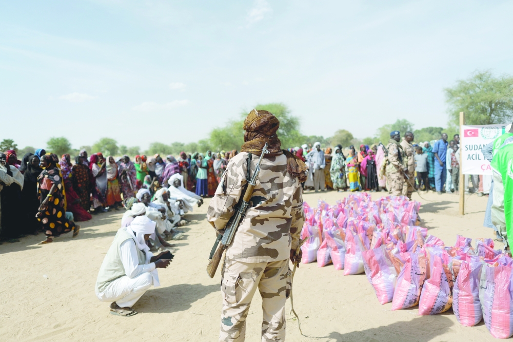 A soldier stands as Sudanese women who fled the violence in their country wait to receive food supplies near Chad borders. — Reuters