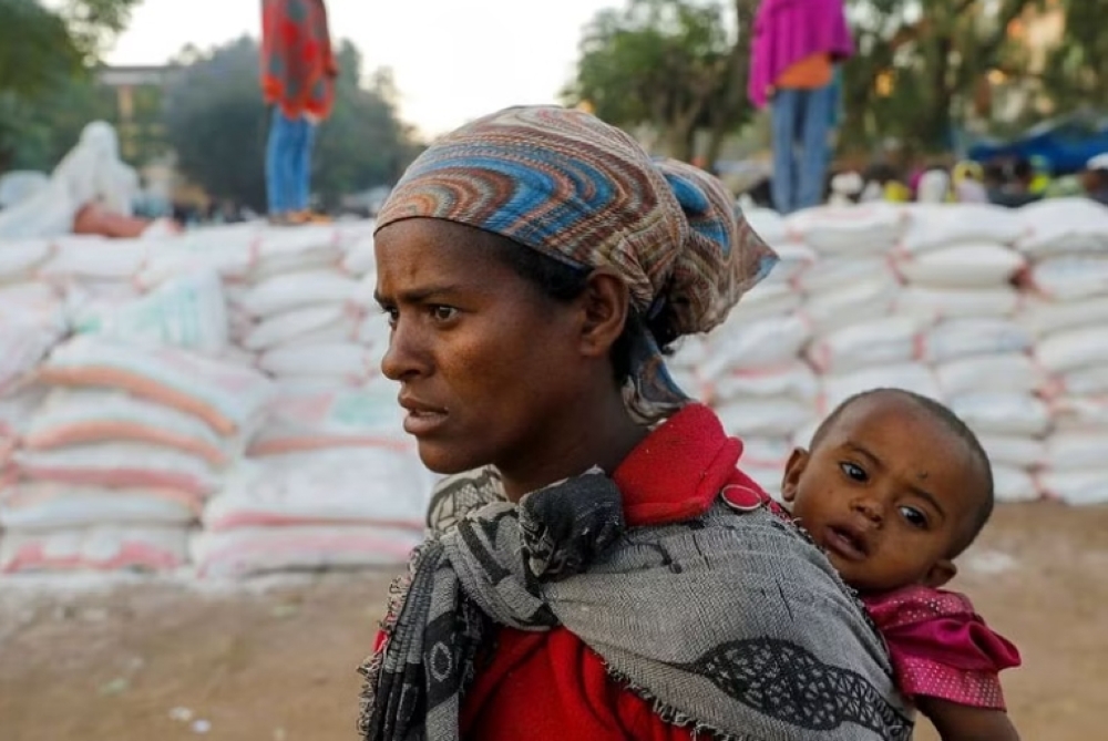 A woman carries an infant as she stands in a line for food at the Tsehaye primary school, in the town of Shire, Tigray region, Ethiopia. - Reuters