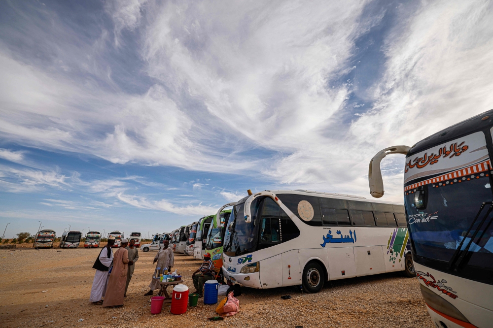Sudanese drivers wait by their buses upon arrival at the Egyptian village of Wadi Karkar near Aswan on May 14, 2023 after fleeing war-torn Sudan. (Photo by Khaled DESOUKI / AFP)

