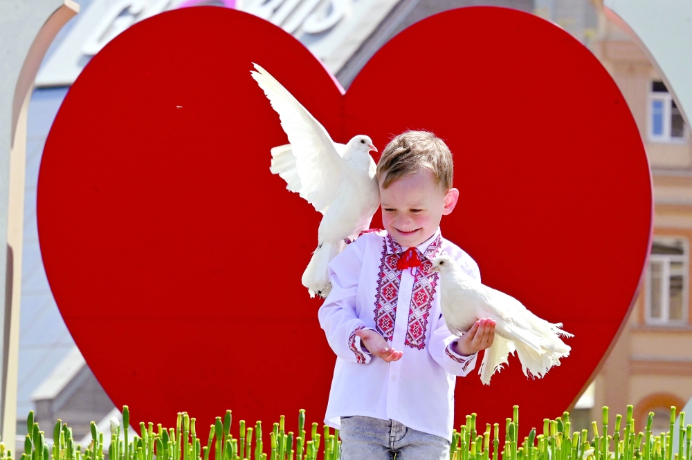 A boy wearing a Vyshyvanka, a traditional Ukrainian embroidered blouse, holds pigeons as he poses for his mother at Independence Square in Kyiv during marking 'Vyshyvanka Day' amid the Russian invasion of Ukraine. - AFP