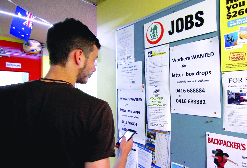 A man uses his phone to record a job add posted on a notice board at a backpacker hostel in Sydney, Australia. - Reuters File 

