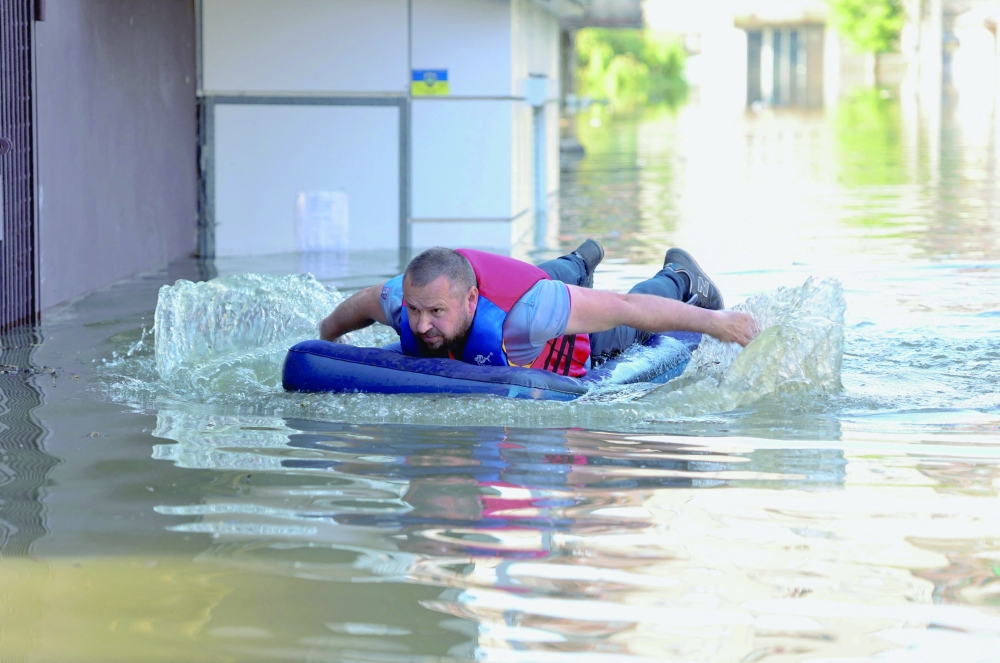 A local resident is seen on an inflatable mattress in a flooded area in Kherson following the destruction of Kakhovka hydroelectric power plant dam. - AFP