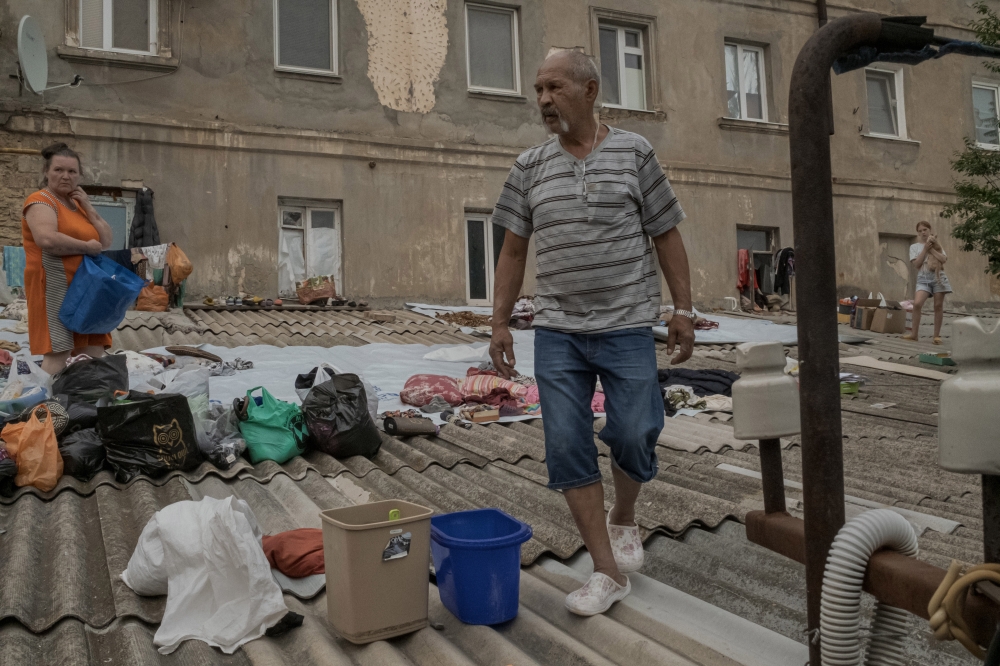 Victor Kopayev, center, and his wife, Galyna, move their belongings to the roof of their flooded house in Kherson, downriver from the destroyed Kakhovka dam, June 7, 2023. (Mauricio Lima/The New York Times)