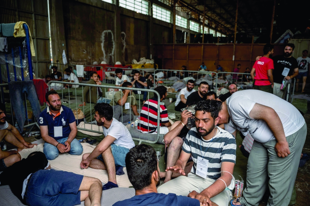 Survivors of a shipwreck sit inside a warehouse at the port in Kalamata town. - AFP
