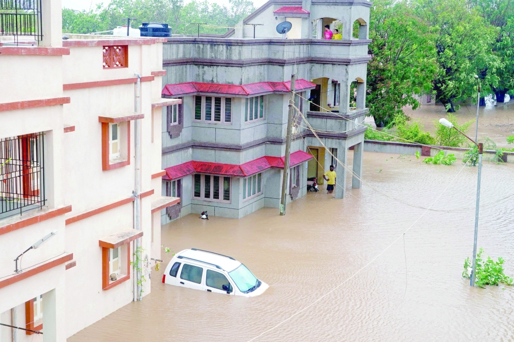 Residents watch as a car drowns in an inundated street at the coastal town of Mandvi as cyclone Biparjoy makes landfall. - AFP