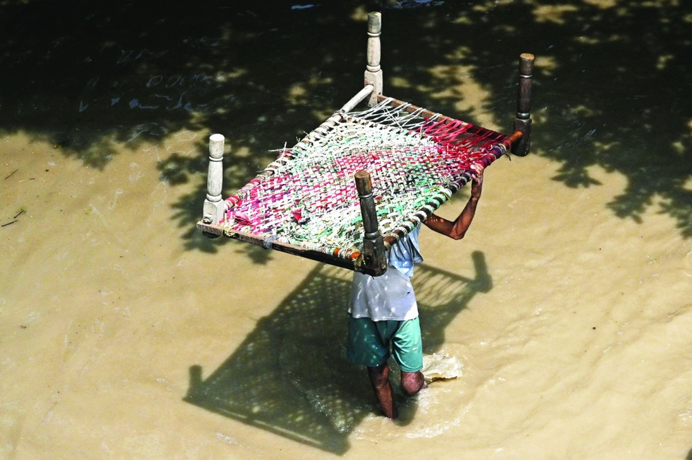A man carries a cot through a flooded street after river Yamuna overflowed following heavy monsoon rains in New Delhi. - AFP
