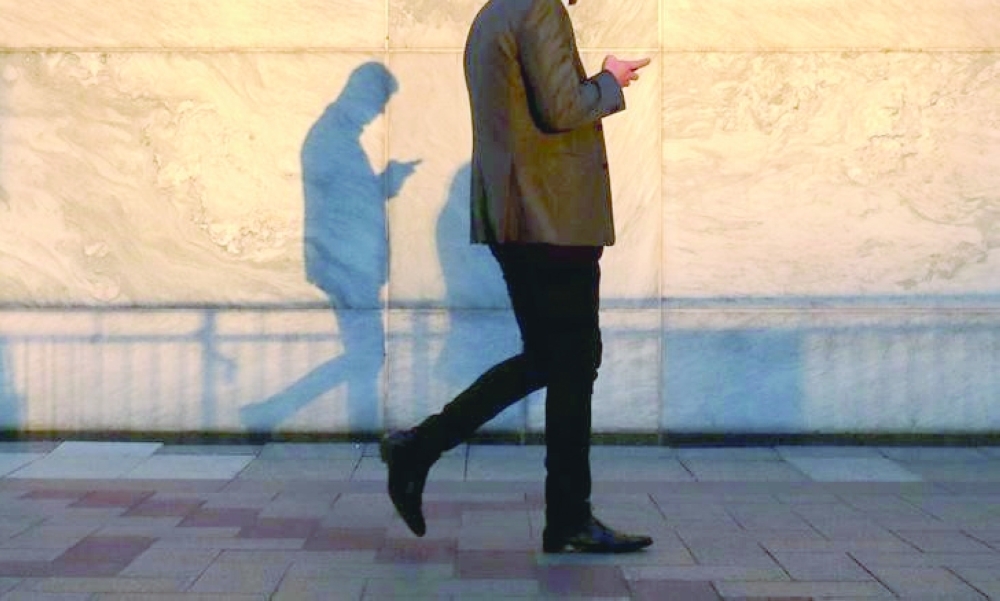 An unidentified man using a smart phone walks through London's Canary Wharf financial district in the evening light in London. — Reuters