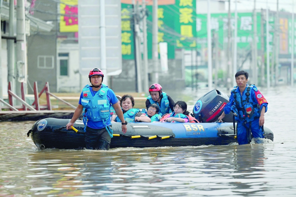 Rescue team personnel wade in a flooded road as they evacuate residents following heavy rains in Zhuozhou. — AFP