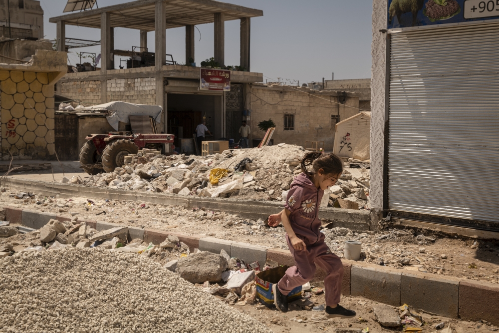 A girl walks in front of the remains of a building that was destroyed in February by the earthquake, in Jindires, Syria, on Aug. 8, 2023. (Nicole Tung/The New York Times)