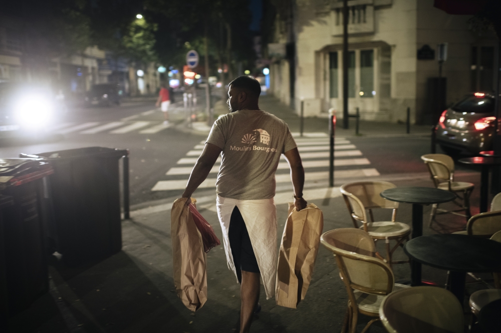 Tharshan Selvarajah, the 2023 winner of the “Grand Prize of the Traditional French Baguette,” carrying paper bags with baguettes made for Élysée Palace outside his bakery, “Au levain des Pyrénées”, in Paris on Sept. 14, 2023. (Dmitry Kostyukov/The New York Times)