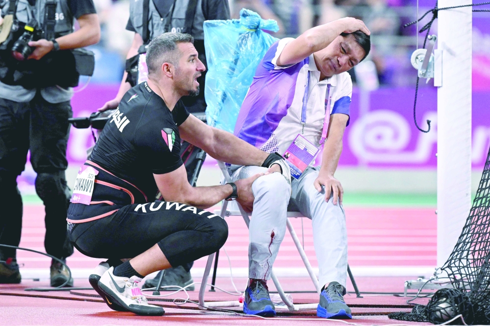 An official reacts after his leg was injured by a stray hammer thrown by Ali Zankawi (L) who attempts to stem the bleeding during the men's hammer throw final athletics event at Hangzhou. — AFP)