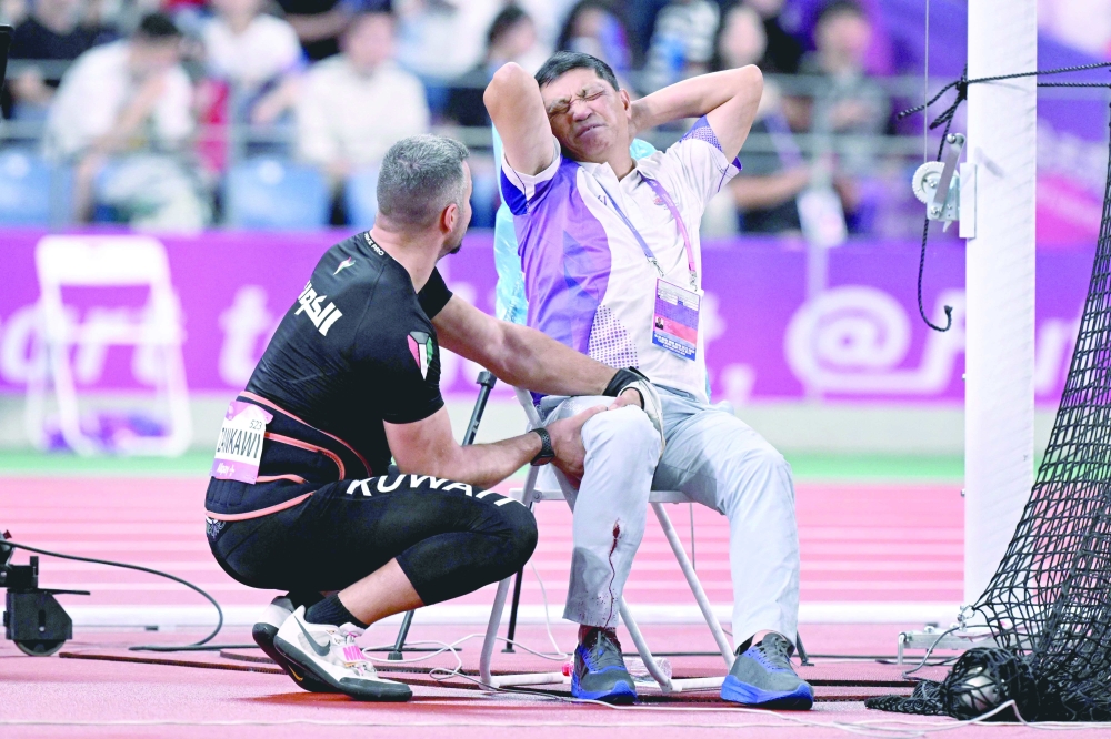 An official reacts in pain after his leg was injured by a stray hammer thrown by Ali Zankawi (L) who attempts to stem the bleeding during the men's hammer throw final in Hangzhou. — AFP
