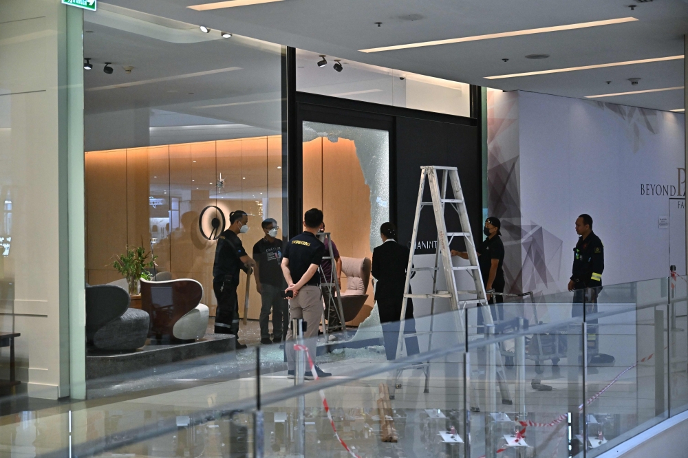 Staff repair the glass doors of a furniture store at the Siam Paragon shopping mall where a 14-year-old suspect was apprehended the night before after a shooting rampage in Bangkok on October 4, 2023. 