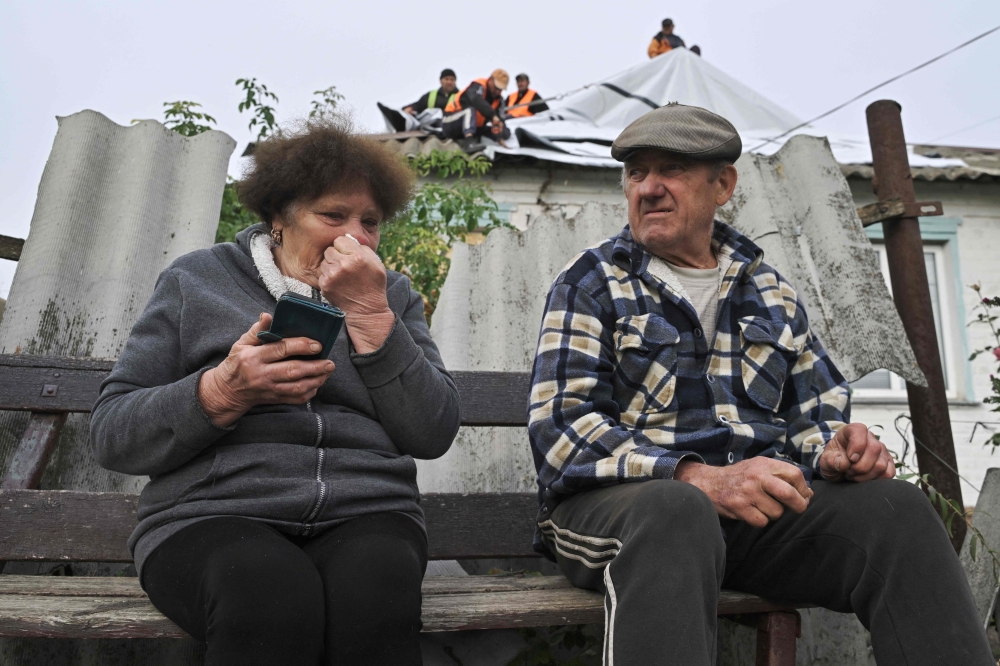 Local resident Valentyna (L), sits with her spouse Volodymyr, 76 in front of their damaged house following a Russian strike which hit a shop and cafe in the village of Groza, 30 kilometres west of Kupiansk. - AFP