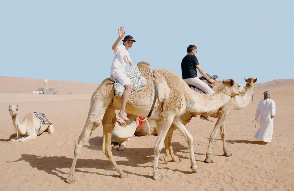 A tourist waves to a camera during a camel ride trip in Oman, in this file photo.