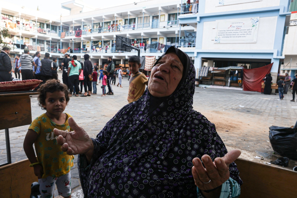 A Palestinian woman looks up as she prays in the yard of a school, in the Rafah refugee camp