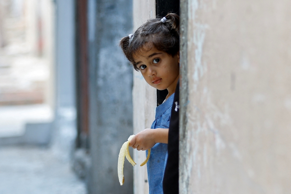 A Palestinian girl holds banana as she looks out of her family house, amid the ongoing Israeli-Palestinian conflict, in Khan Younis refugee camp in the southern Gaza Strip October 14, 2023. REUTERS/Ibraheem Abu Mustafa