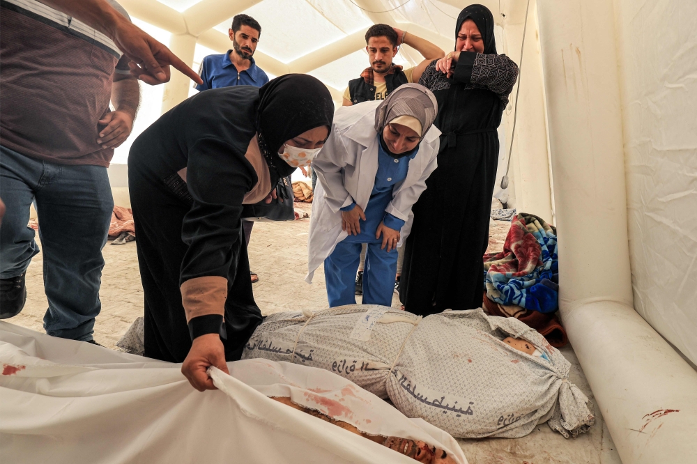 People inspect to identify one of the bodies of victims of the overnight blast at the Ahli Arab hospital at a makeshift tent at the site in central Gaza on October 18