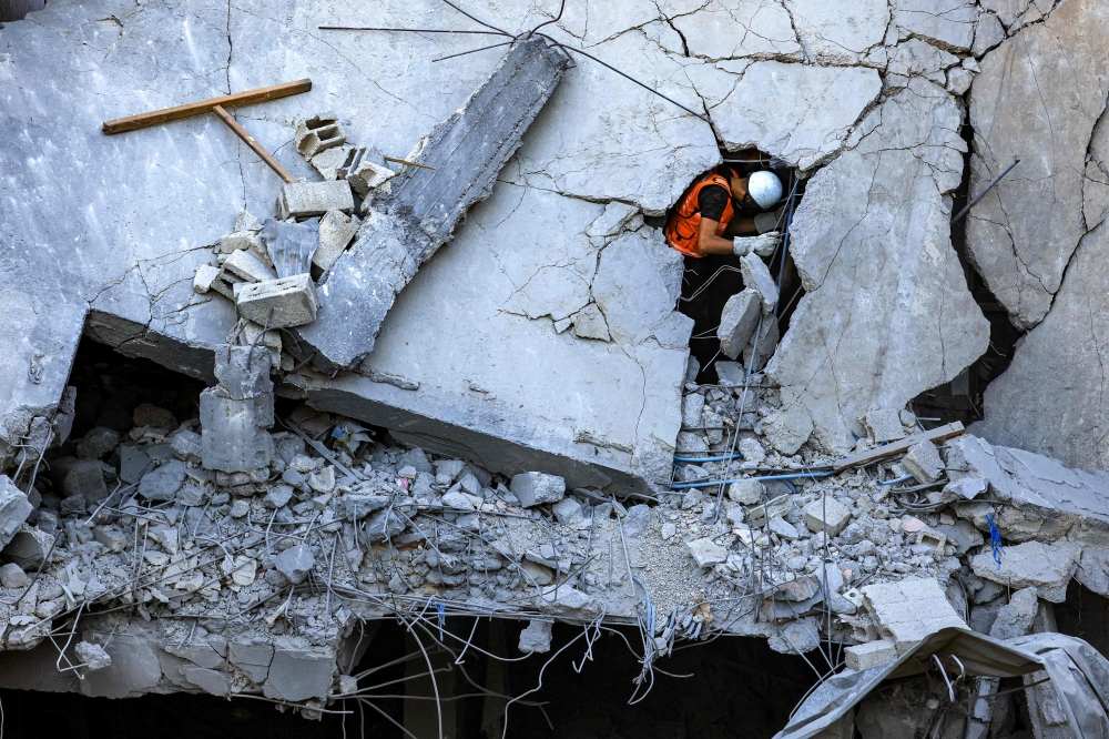 A Palestinian civil defence member stands through a crack in a collapsed building hit by Israeli bombardment while searching for victims and survivors, in Khan Yunis in the southern Gaza Strip on Thursday. — AFP