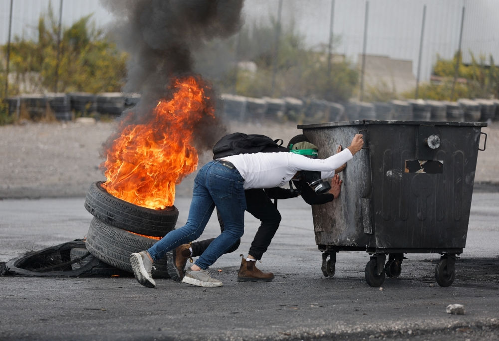 Palestinians hide behind a container during clashes with Israeli forces near Ramallah in the Israeli-occupied West Bank 