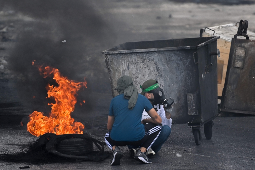 Palestinian youths use rubbish containers for cover during clashes with Israeli security forces 