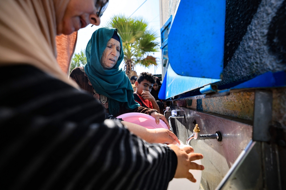 Displaced people fetch drinking water in the yard of a United Nations Relief and Works Agency for Palestine Refugees (UNRWA) school in Khan Yunis. - AFP
