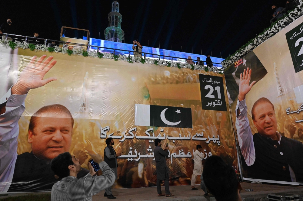 Supporters of Nawaz Sharif gather beside large banners of Sharif's displayed at a welcoming stage at a park ahead of his arrival in Lahore on October 20, 2023. 