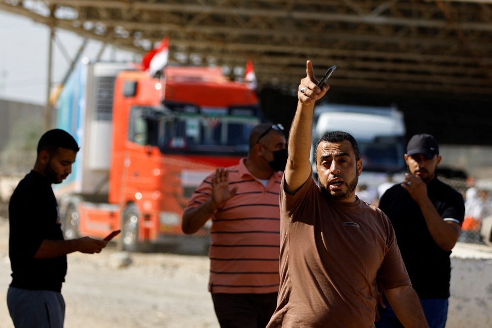 Workers gesture as trucks carrying aid arrive at the Palestinian side of the border with Egypt