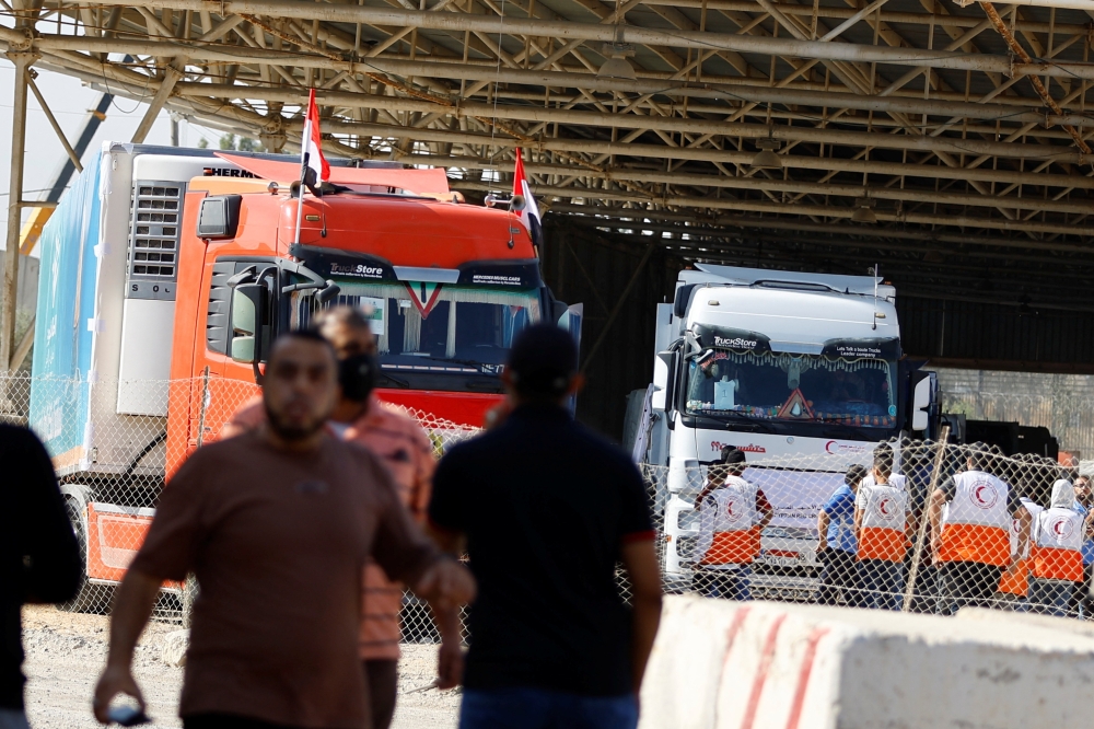 Workers gather as trucks carrying aid arrive at the Palestinian side of the border with Egypt