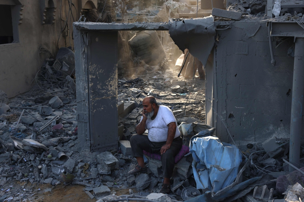 TOPSHOT - A Palestinian man sits on the debris of a house after overnight Israeli strikes on Rafah in the southern Gaza Strip on October 22, 2023 amid the ongoing battles between Israel and Palestinian groups. Overnight raids on the Gaza Strip killed at least 55 people, the Hamas government said on October 22, after Israel announced it was stepping up strikes. (Photo by SAID KHATIB / AFP)
