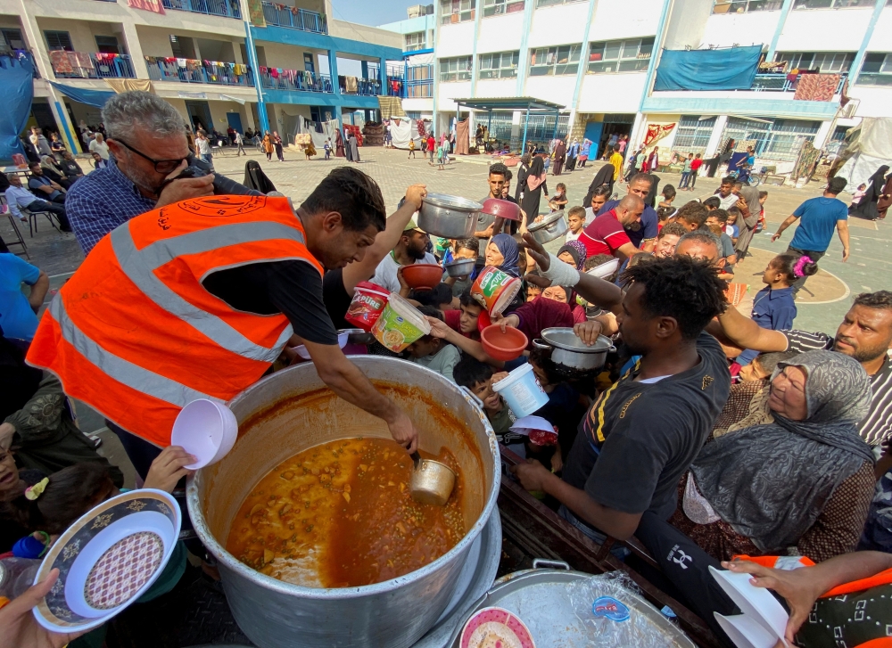 Palestinians, who fled their houses due to Israeli strikes, gather to get their share of charity food offered by volunteers
