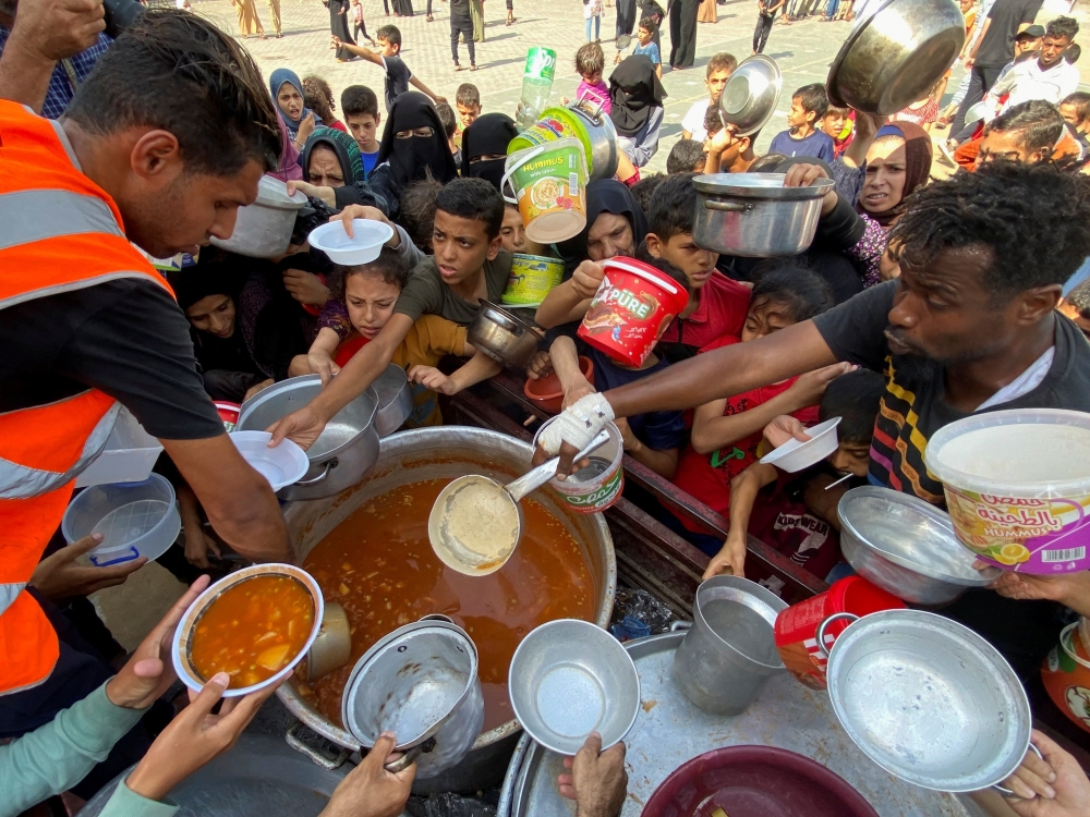 Palestinians, who fled their houses due to Israeli strikes, gather to get their share of charity food offered by volunteers
