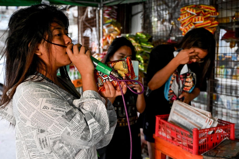 This photo taken on October 3, 2023 shows a woman singing from a karaoke machine in Baseco, Manila. Karaoke is wildly popular in the archipelago nation where it's never too early -- or too late -- to grab a microphone and sing a tune. Machines can be found everywhere from dingy bars in far flung towns to modern KTV joints in the capital, and many families have their own or rent one for parties. 
