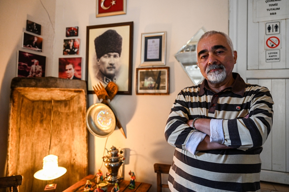 Turkish cafe owner Erdal Erdurk poses next to a portrait of founder of modern Turkey Mustafa Kemal Ataturk at his cafe in Kemaliye, eastern Turkey, on October 4, 2023. Founder of modern Turkey Mustafa Kemal Ataturk rewarded the loyalty of the Kemaliye town, nestled between the mountains and the sources of the Euphrates, by giving it his name ahead of creating the Turkish republic out of the ashes of the Ottoman Empire 100 years ago. (Photo by Ozan KOSE / AFP)

