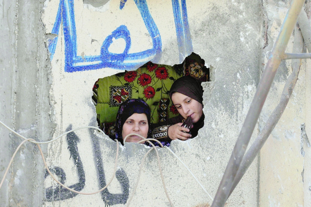 Palestinian women look from a hole in a damaged wall following Israeli strikes on the Rafah refugee camp in the southern Gaza Strip on Wednesday. - AFP