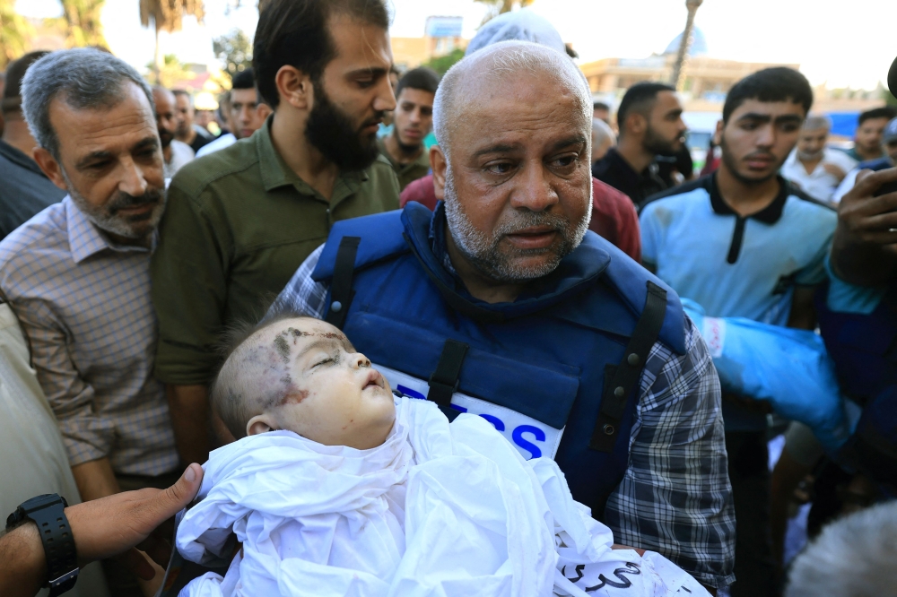  Al-Jazeera correspondent Wael Al-Dahdouh carries the shrouded body of one of his children who was killed along with his wife the day before in an Israeli strike on the Nuseirat camp