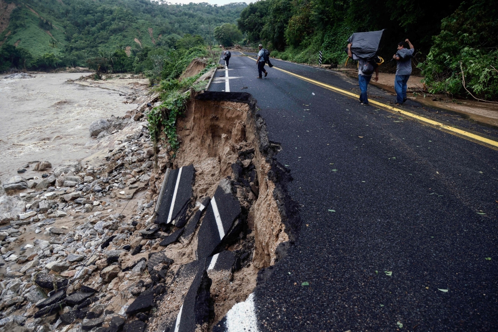 People pass by part of a road which was washed away at the Kilometro 42 community, near Acapulco, Guerrero State, Mexico, after the passage of Hurricane Otis. - AFP
