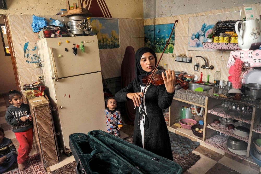 Palestinian musician Jawaher al Aqraa plays a violin as she stands in the kitchen of her home in Deir al Balah in central Gaza Strip. - AFP 