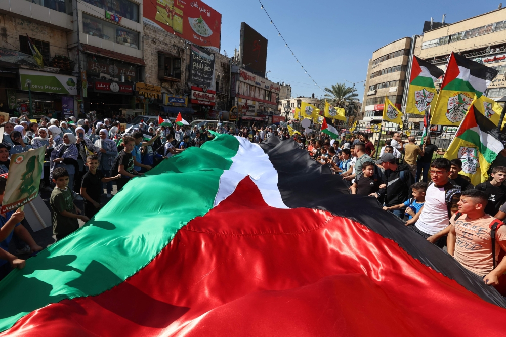 People deploy a large Palestinian flag as they march in support of the people in the Gaza Strip in the occupied West bank city of Nablus. - AFP 