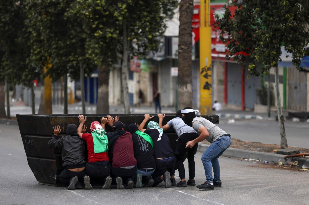 Palestinian youths hide behind a skip as they clash with Israeli forces following a solidarity march with the Palestinians of the Gaza Strip, in the occupied West Bank city of Hebron. - AFP
