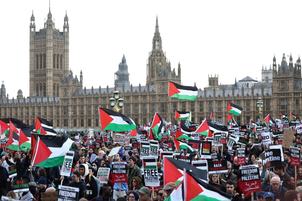 Protesters hold placards and wave Palestinian flags as they walk over Westminster Bridge with the Palace of Westminster, home of the Houses of Parliament behind during a 'March For Palestine' in London. — AFP 