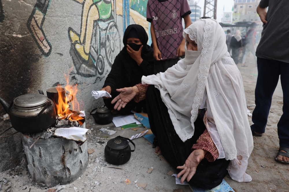 Women burn paper to heat water for tea in Rafah in the southern Gaza Strip 