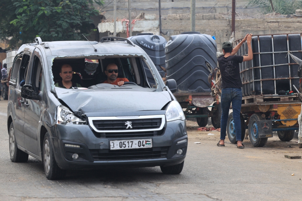 Palestinian men drive a vehicle with a shattered front window screen